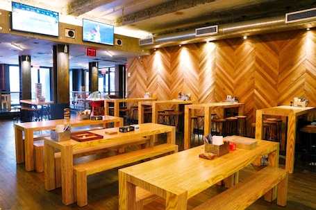 A restaurant with wooden tables and benches, a herringbone-patterned wall, and multiple screens on the ceiling.