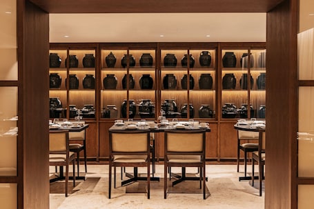 A dining area with wooden tables and chairs, a wall of ceramic vases, and a tiled floor.