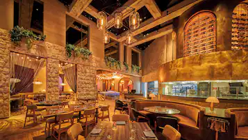 A spacious restaurant with high ceilings, exposed beams, and a wine cellar visible through a glass wall.