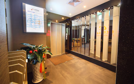 A hotel reception area with a digital map display, a reception desk, a potted plant, and a mirror reflecting the interior.