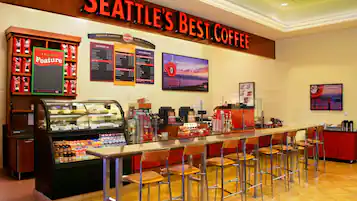 A coffee shop with a long counter, bar stools, and a display case with snacks.