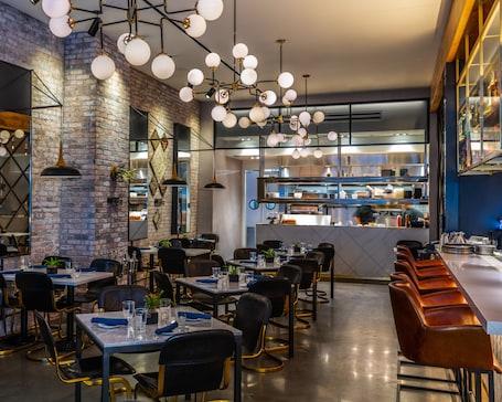 A restaurant interior with brick walls, hanging spherical light fixtures, and a visible kitchen area.