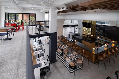 A modern restaurant with multiple dining areas, a central bar, and a staircase leading to an upper level.