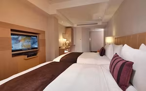 A hotel room with a large bed, a TV mounted on the wall, and a bedside table with a lamp.