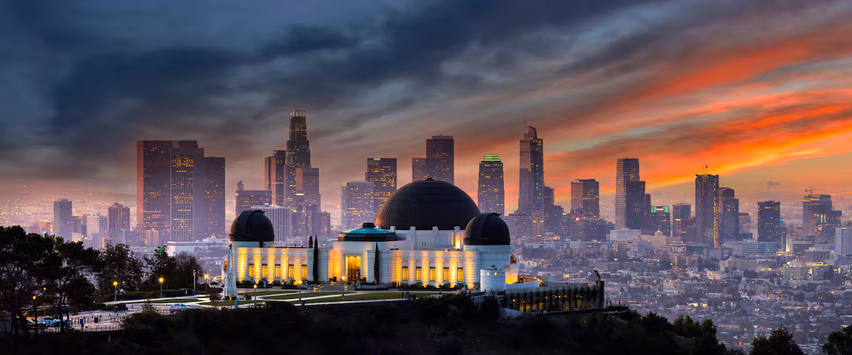 A cityscape with a prominent dome structure and skyscrapers against a sunset sky.